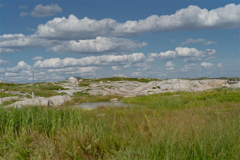 The view behind of Peggy's Cove Lighthouse, which is a field with some rocks.