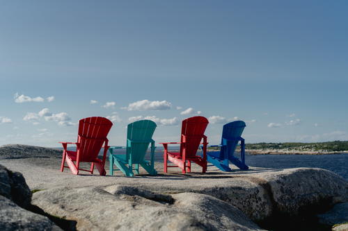 4 chairs (red, teal, red, blue) on top of a rock at Peggy's Cove.