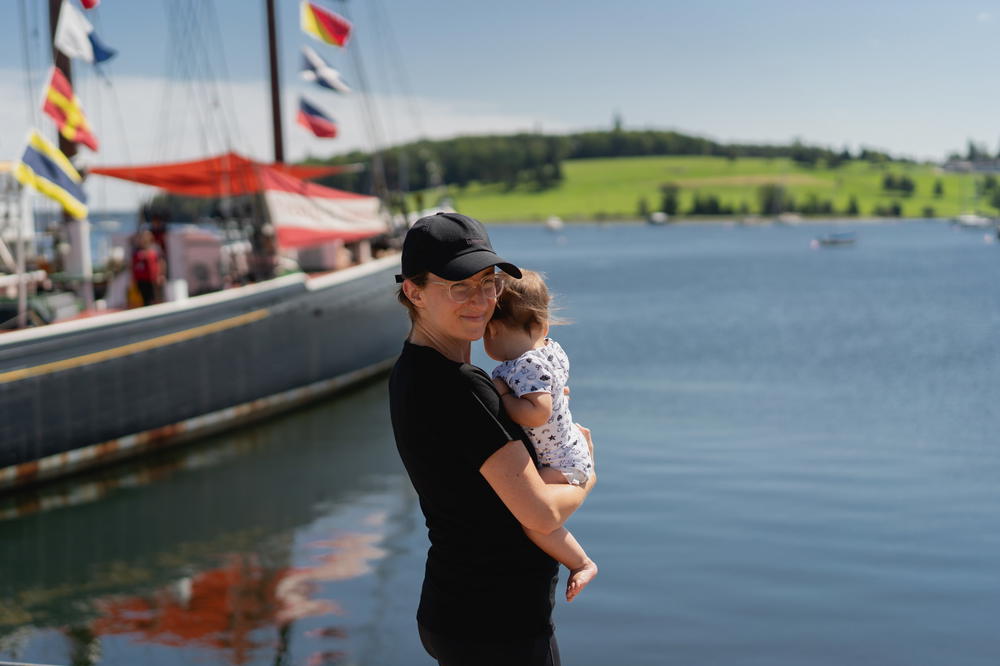 A woman holding a baby in front of a boat in Halifax, Canada.