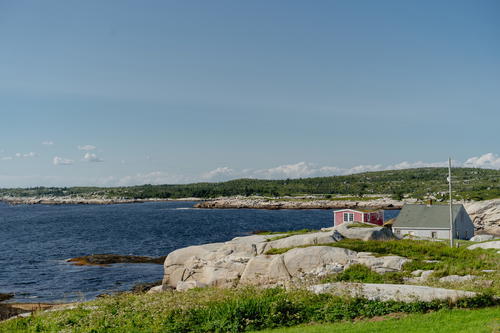 A small red house sits on top of a rocky cliff overlooking the ocean in Halifax, Canada.