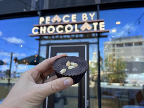 A person in Halifax, Canada holding up a chocolate cupcake in front of Peace by Chocolate.