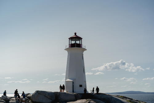 A group of people standing on top of a rock next to a light house