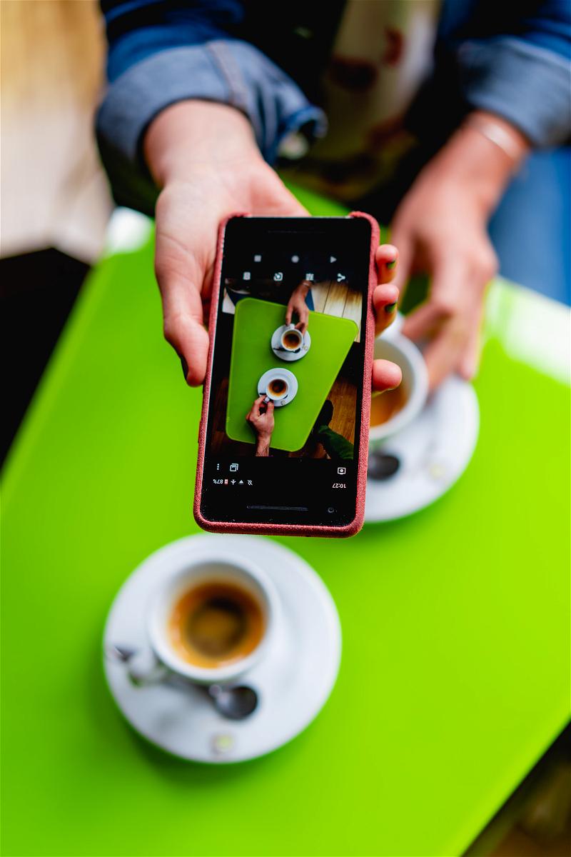 Woman holding Google Pixel phone to take a photo of two cups of coffee on a bright green table