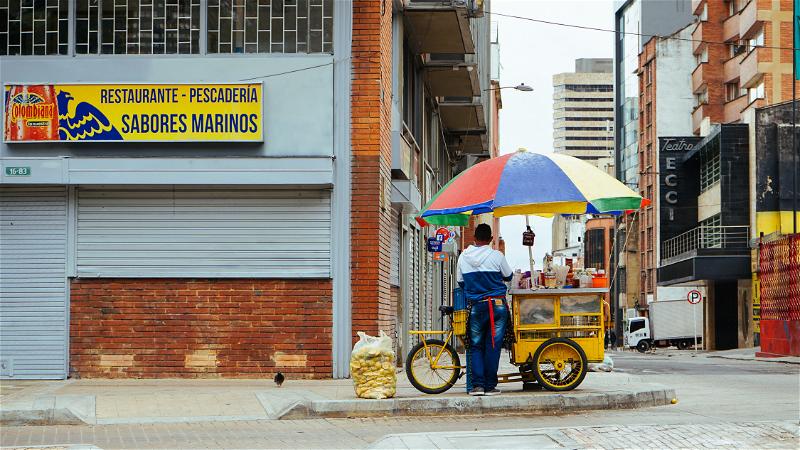 A woman selling food on a cart on the side of a street.