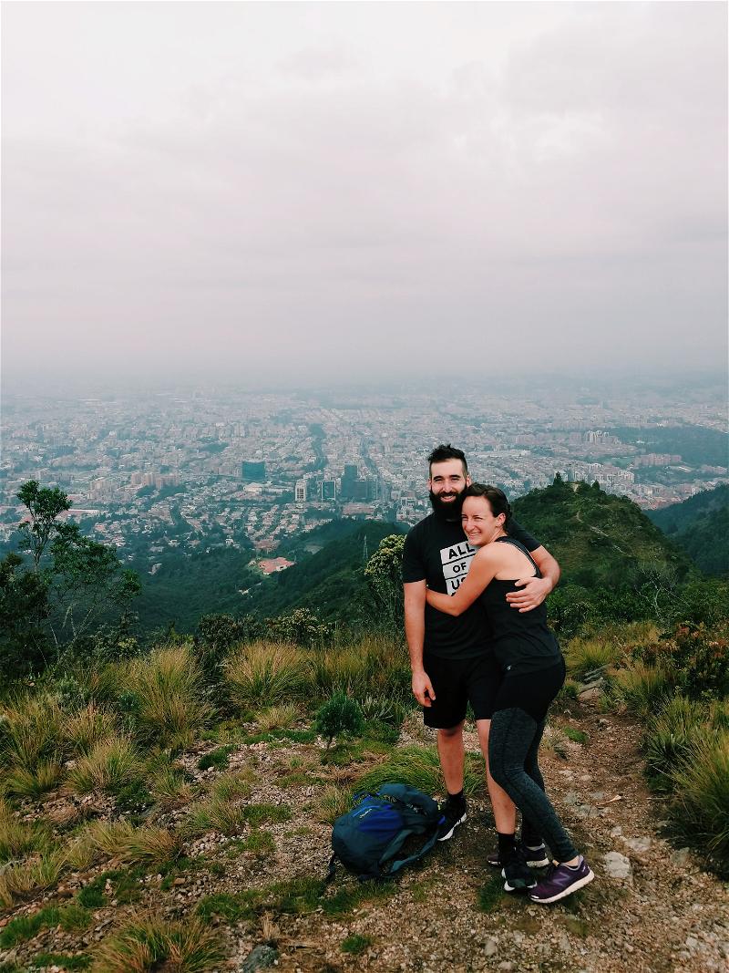 A man and woman hugging on top of a mountain.
