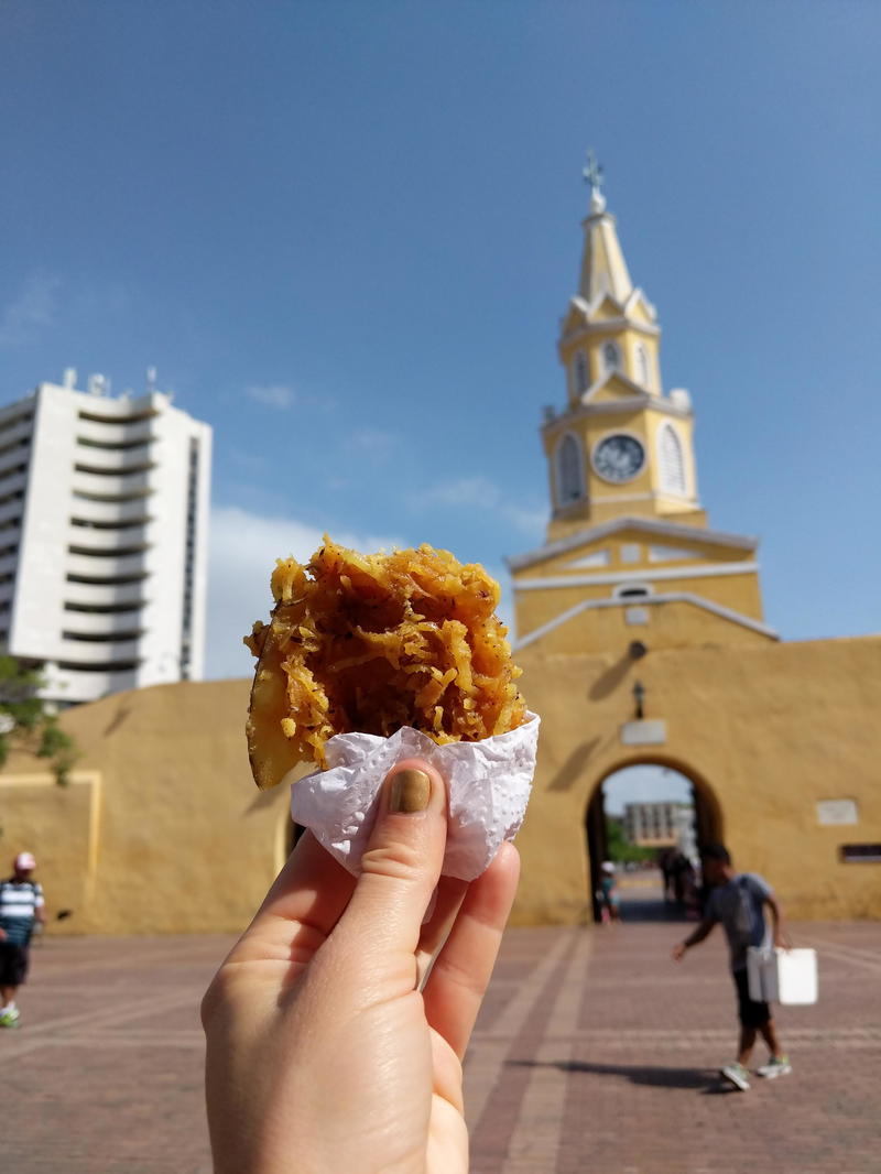 A person holding a piece of food in front of a building.