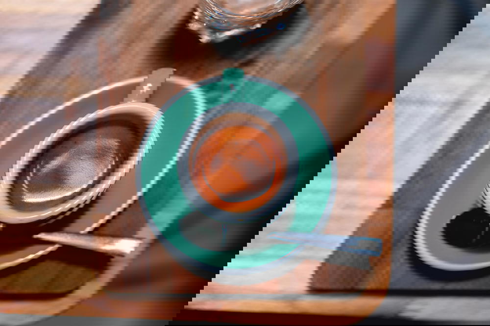 Turquoise saucer and espresso cup filled with espresso on a wooden table in a coffee shop