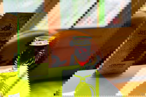 A glass of coffee on a table in front of a window.