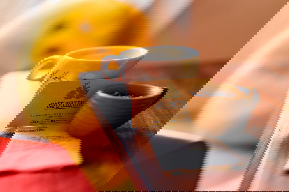 White coffeecup next to a cafe business card and brown espresso cup full of coffee beans from Colombia