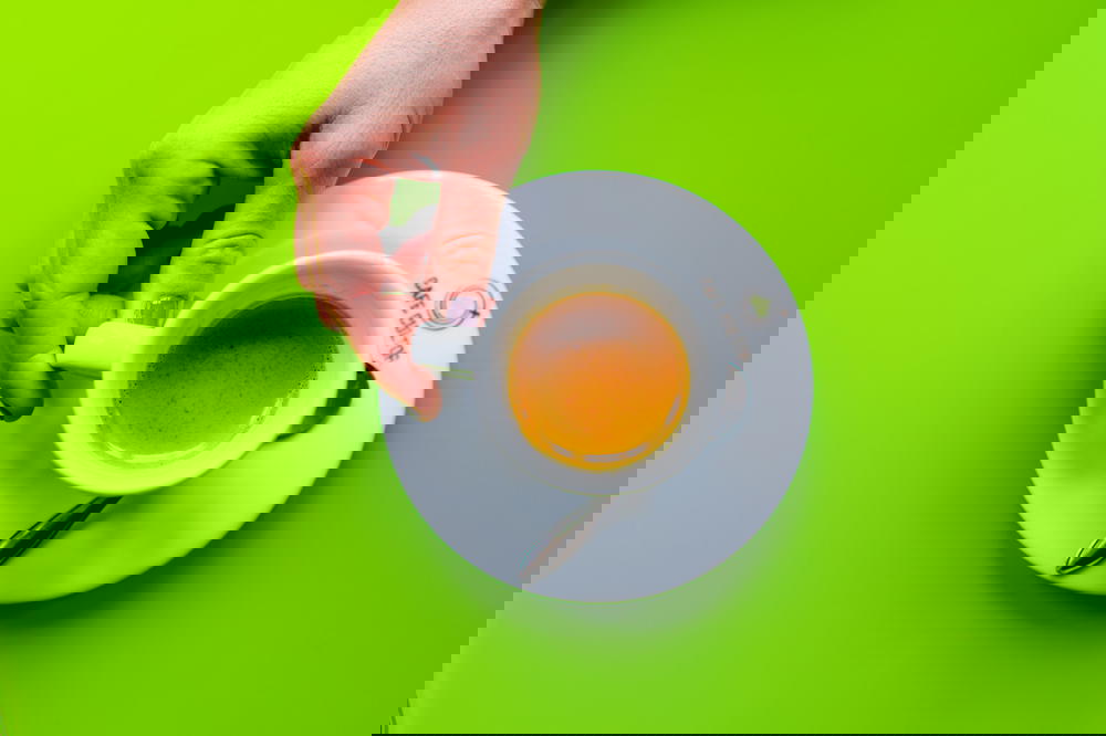 Girl holding the handle of a white espresso cup on a white saucer against a lime green table surface at a cafe
