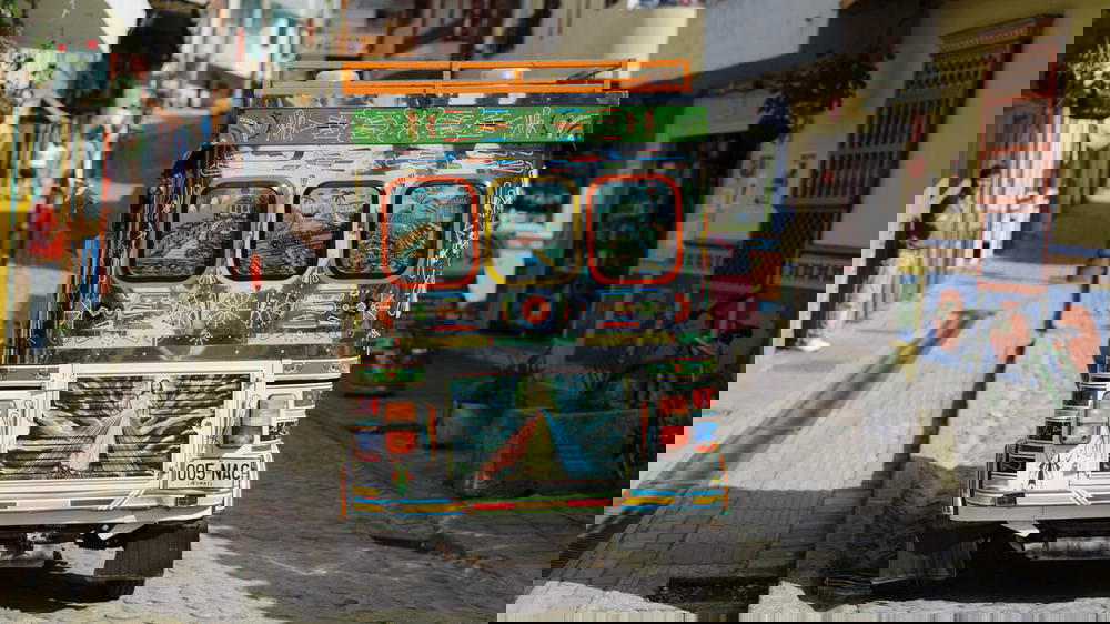 A colorful tuk tuk driving down a cobblestone street.