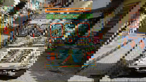 A colorful tuk tuk driving down a cobblestone street.