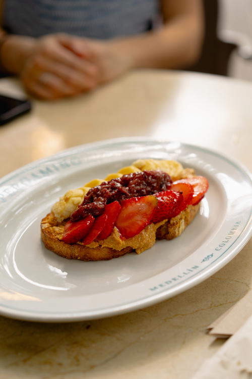 A white plate with peanut butter toast with fruit on top