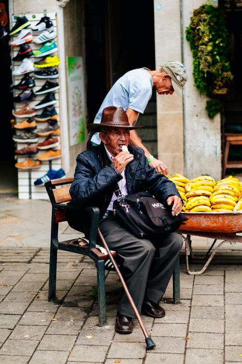 A man sitting on a bench next to a pile of bananas