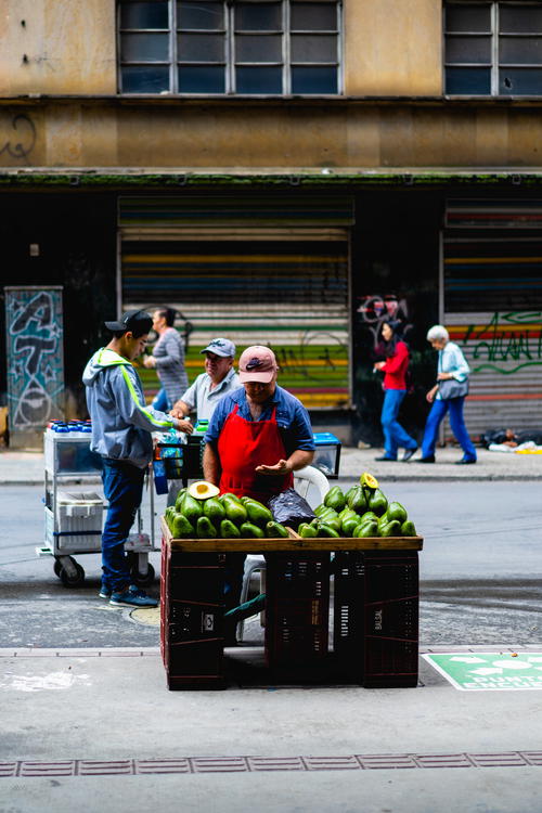 A man standing next to a cart filled with lots of green fruit