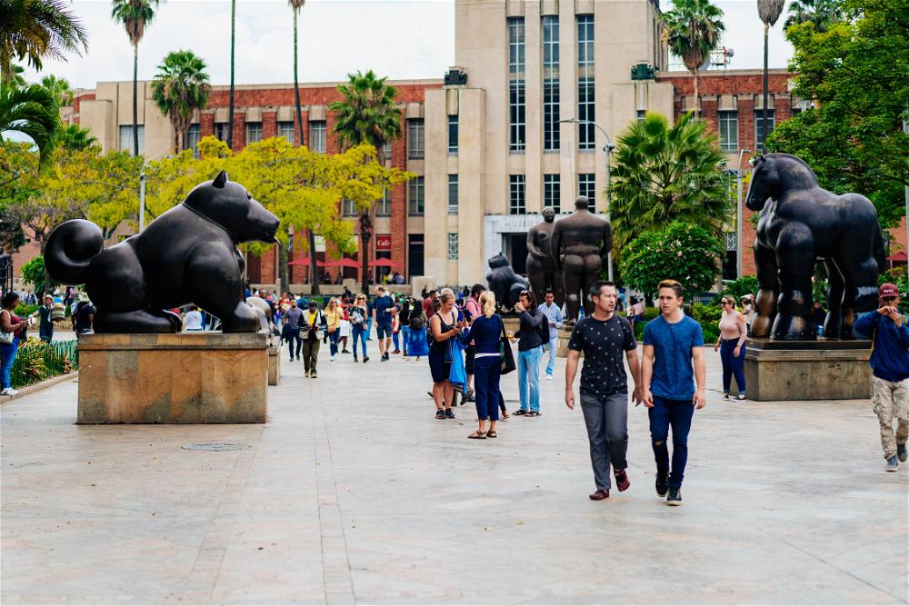 A group of people walking through a plaza with statues of horses.