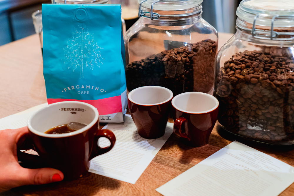 A person holding a cup of coffee next to a bag of coffee beans.