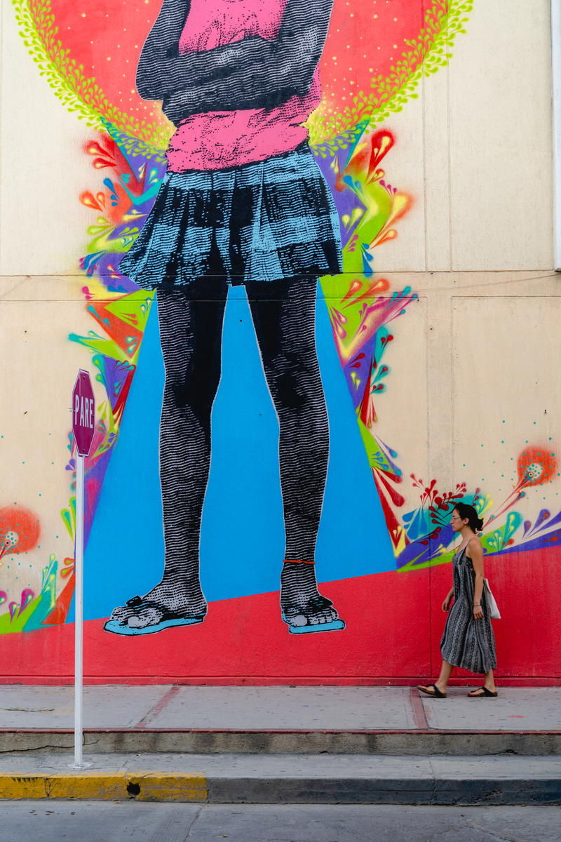 A woman walking down the street near a colorful mural.