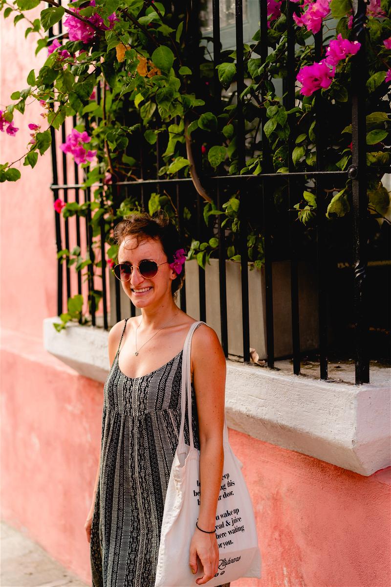 A woman wearing sunglasses and a black dress in front of a pink building.
