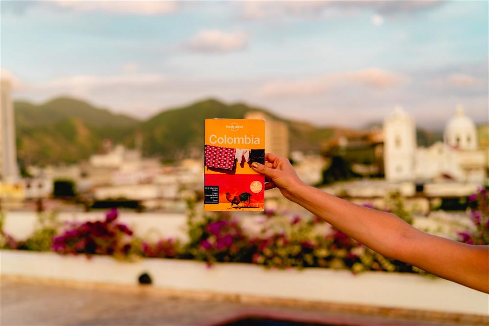A woman holding up a book on a rooftop with a view of a city.