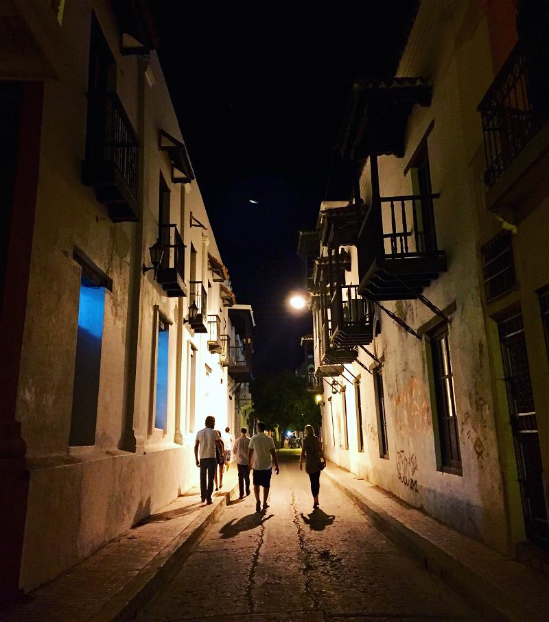 Three people walking down a cobblestone street at night.