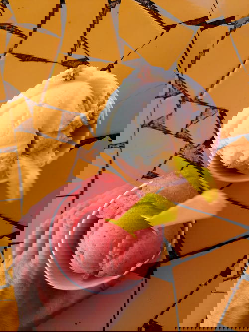 Womans' hand holding a paper cup of strawberry sorbet with a yellow plastic spoon