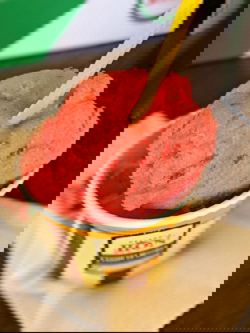 Strawberry sorbet in a small paper cut with a plastic yellow spoon
