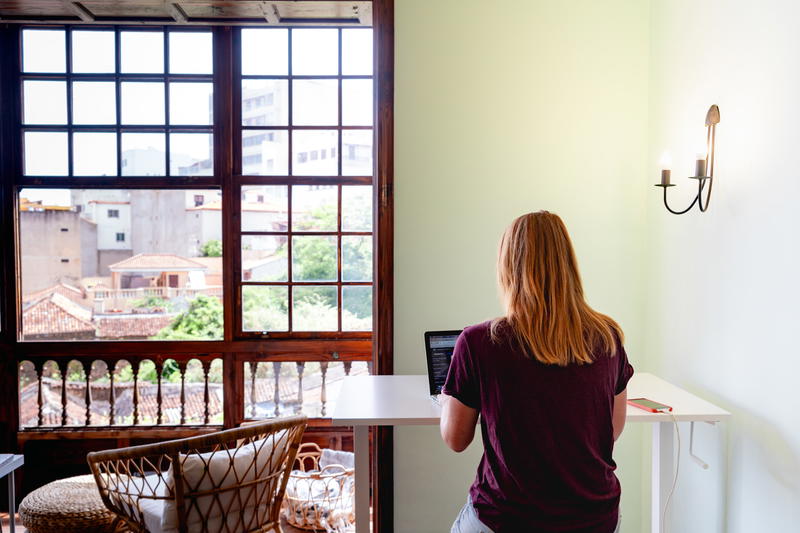 A woman working on a laptop in a room with a window.