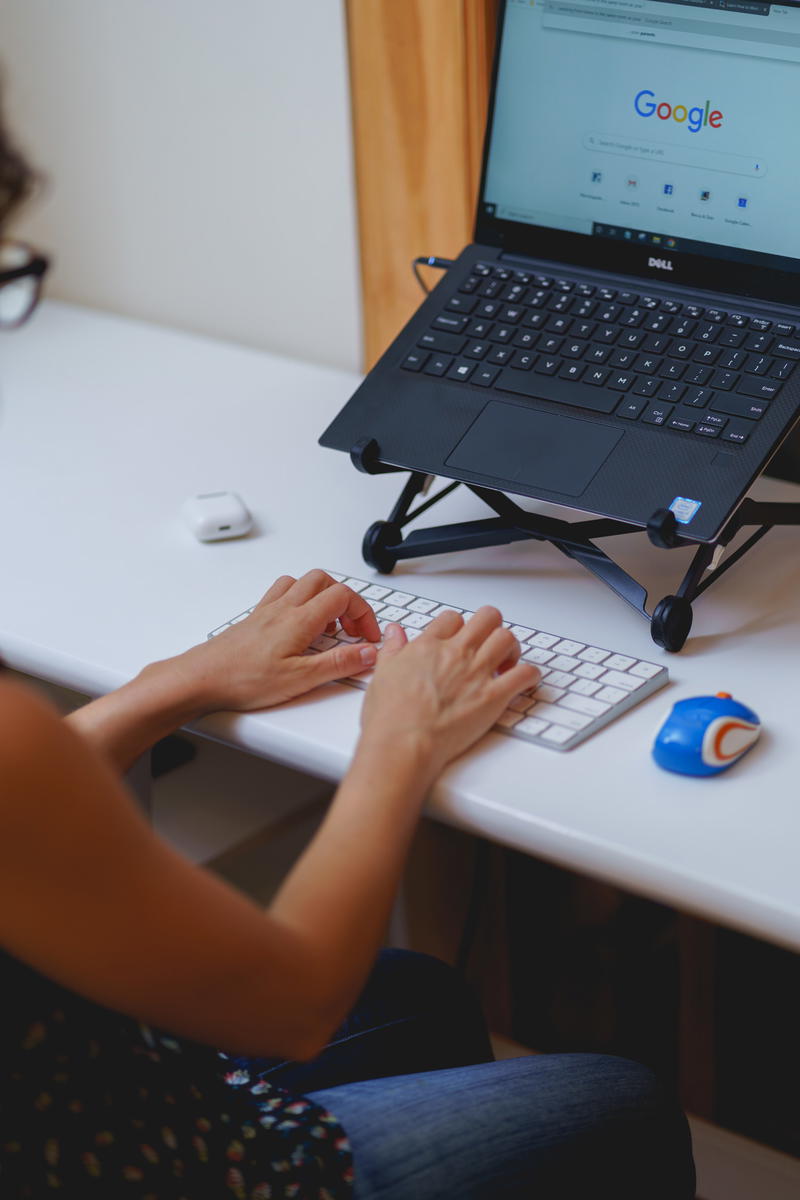 Typing and working from home at a laptop with a Roost laptop stand and external keyboard at a small desk