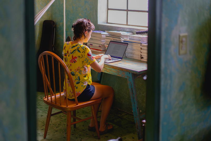 A woman working on a laptop in a small room.