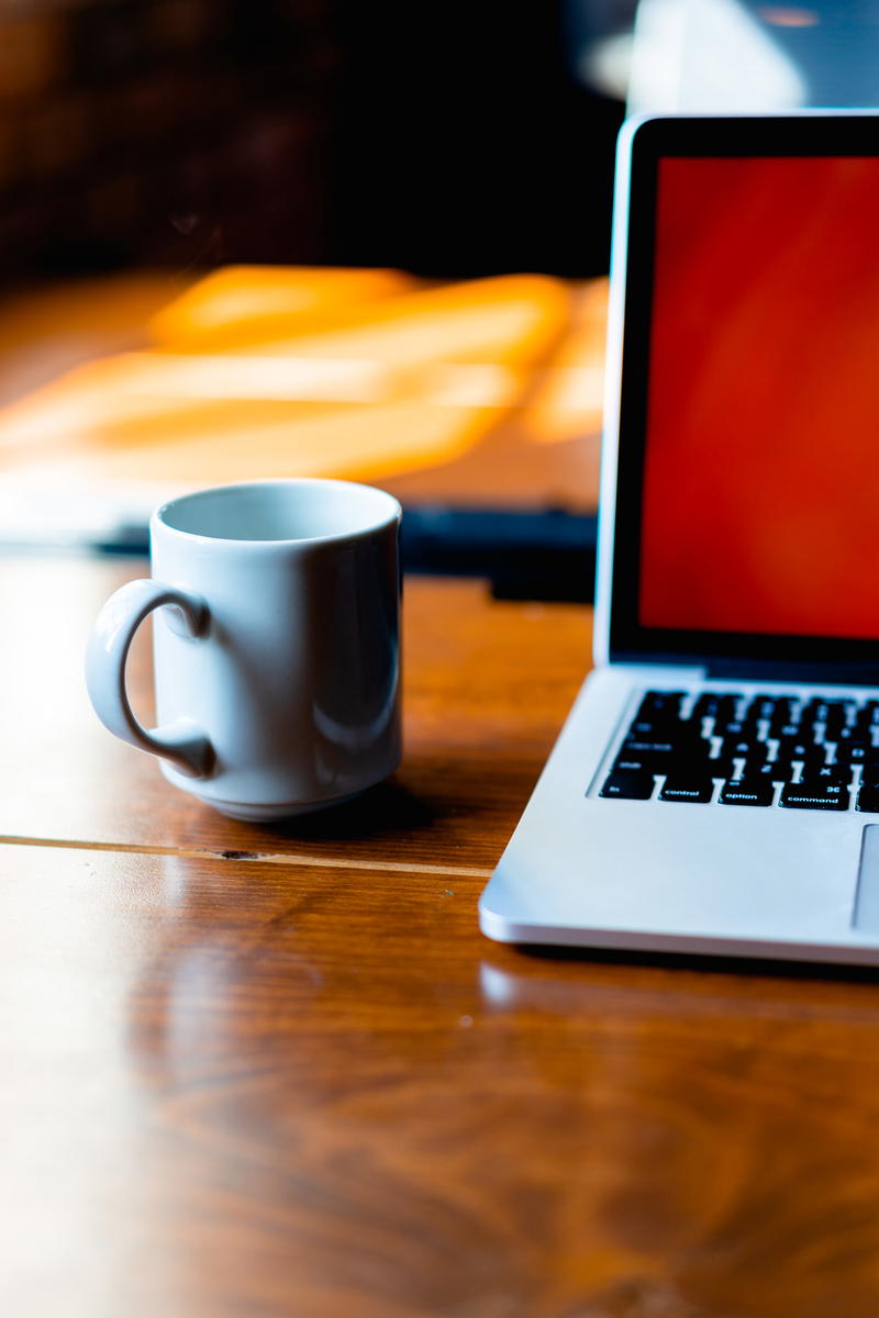 A laptop computer on a table next to a cup of coffee.