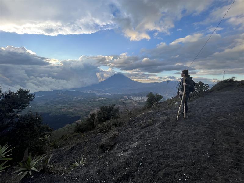 A person is standing on a mountain with a view of a volcano.