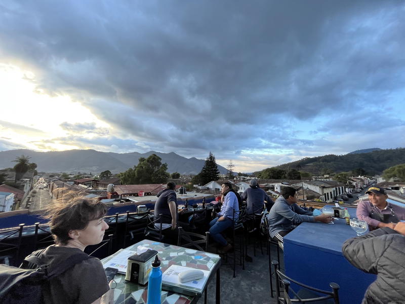 A group of people sitting at tables on a rooftop with mountains in the background.