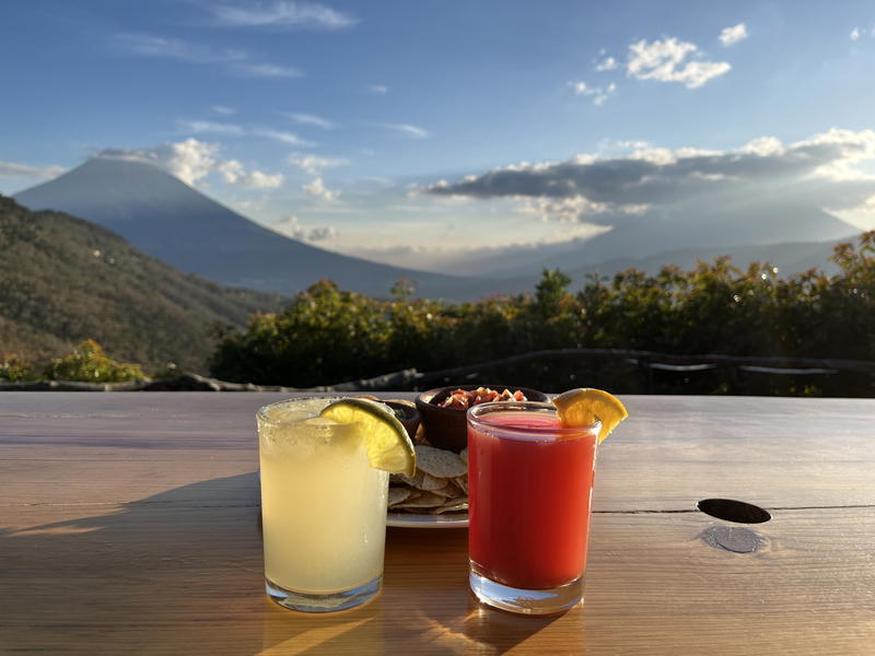 Two drinks on a wooden table in front of a mountain in Guatemala.