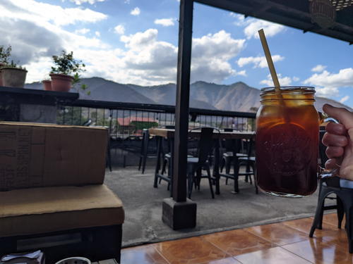 A person enjoying a glass of iced coffee in Guatemala with mountains in the background.