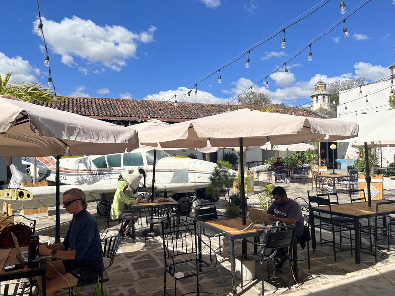 A restaurant with tables and umbrellas in front of a Guatemalan plane.