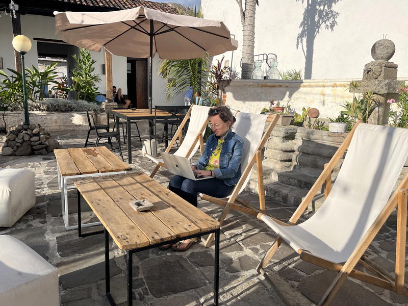 A man in Hong Kong sits on a wooden deck chair with a laptop on his lap.