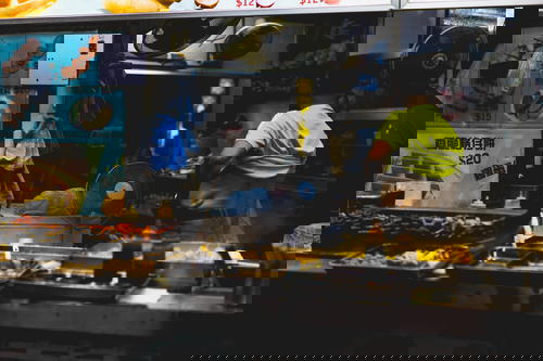 A man in Hong Kong standing in front of a food stall.