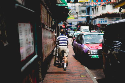 A man cycling down a narrow street in Hong Kong.