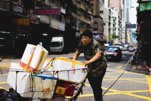 A man pushing a cart full of boxes on a lively Hong Kong street.