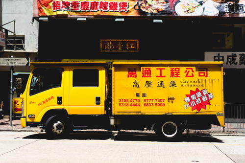 A yellow truck parked in front of a building in Hong Kong.