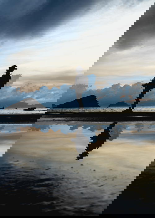 A silhouette of a person standing on a beach at sunset in Hong Kong.