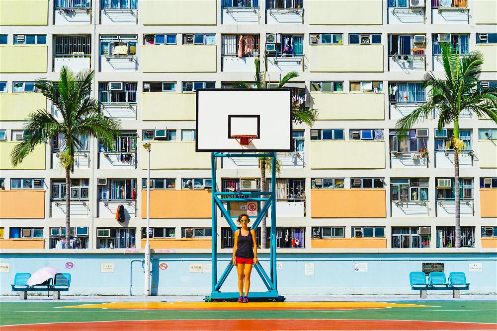 A girl is playing basketball in front of an apartment building in Hong Kong.