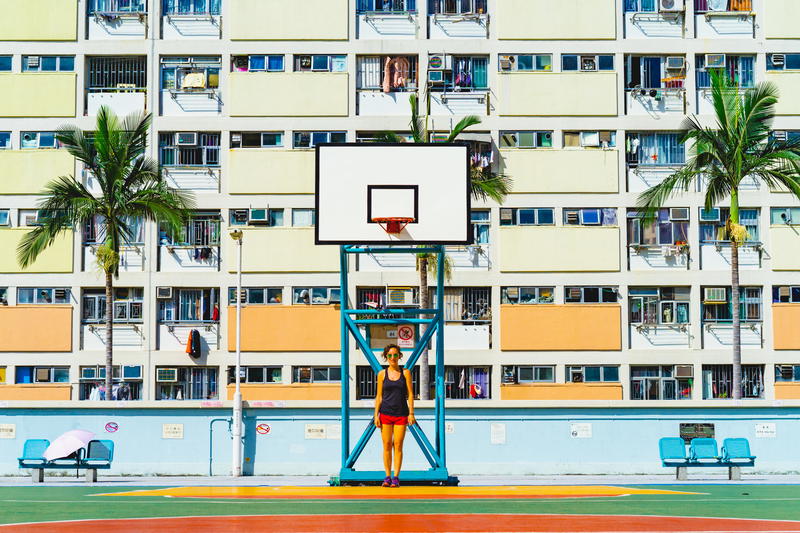 A girl is playing basketball in front of an apartment building in Hong Kong.