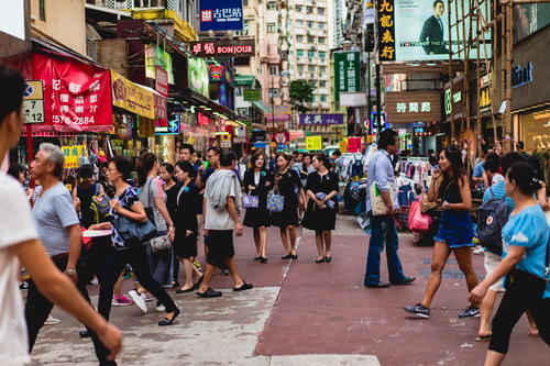 A crowd of people walking down a street in Hong Kong, an asian city.