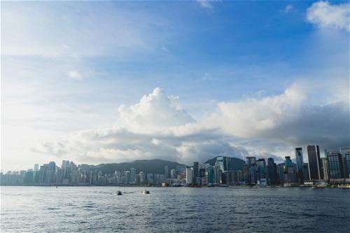 A Hong Kong skyline against a blue sky with white clouds.