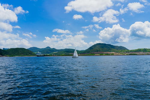 A sailboat in Hong Kong waters with mountains as a backdrop.