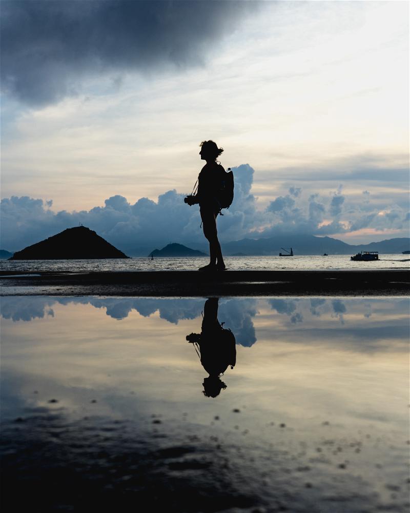A silhouette of a person standing on a Hong Kong beach at sunset.