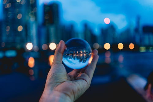 A person holding a glass ball in front of the dynamic cityscape of Hong Kong.