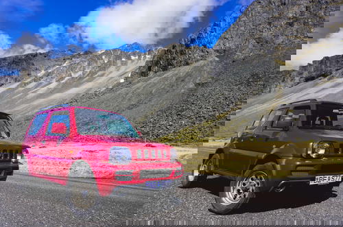 A red SUV is parked in front of a mountain in Iceland.